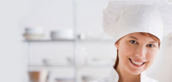 A woman is wearing a chef 's hat and smiling.