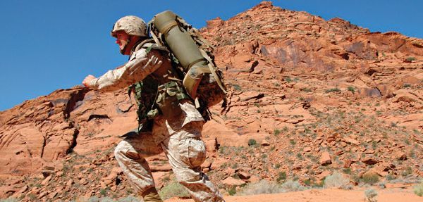 A soldier with a backpack is walking up a mountain.