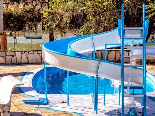 Um toboágua azul e branco se curva em direção a uma piscina. Uma escada leva ao topo.