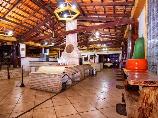 Interior amplo e rústico de restaurante com lareira de tijolos e assentos. Uma cabaça decorativa sobre uma mesa de madeira.