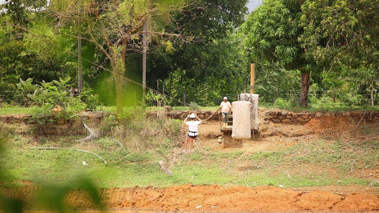 Duas pessoas perto de uma estrutura de concreto em uma área rural com árvores e um barranco gramado.