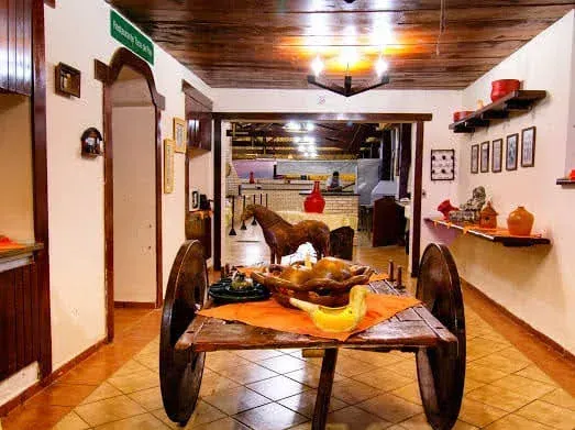 Vista interna de uma sala rústica com uma mesa de carrinho de madeira, um cavalo de brinquedo e um vislumbre de outra sala ao fundo.