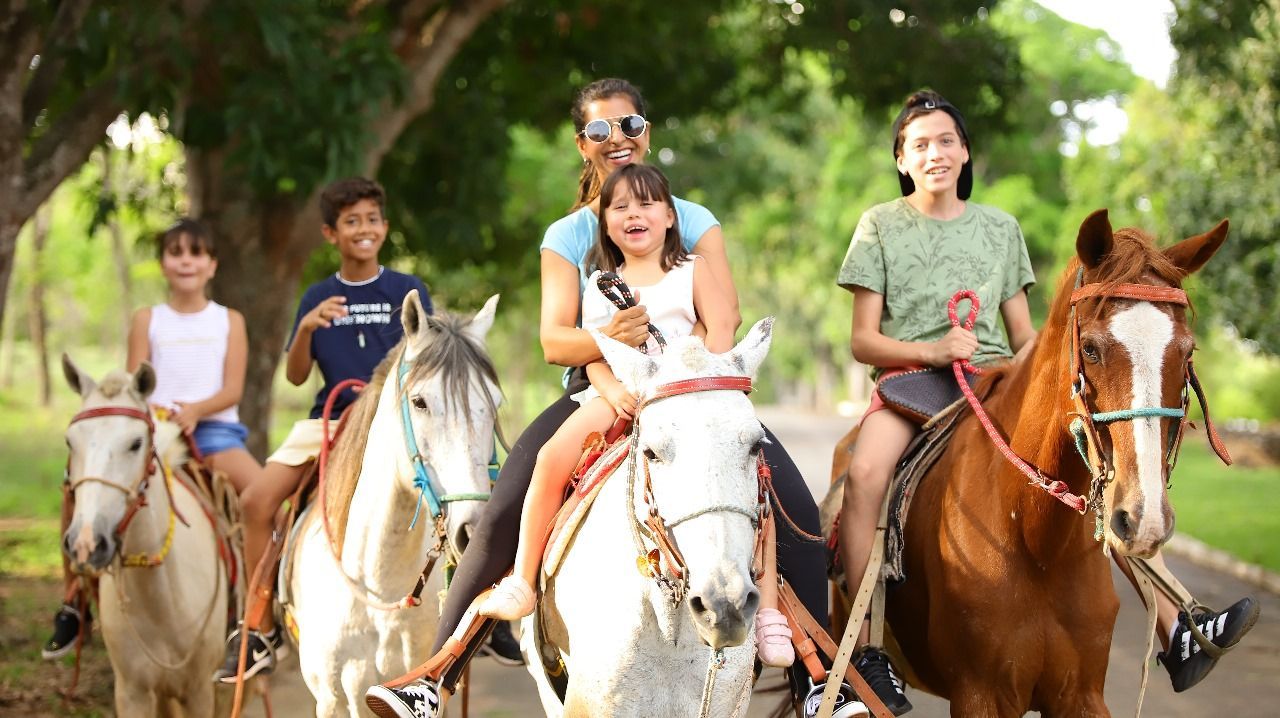 Um grupo de cinco pessoas, sorrindo, cavalgando por uma trilha em um parque.