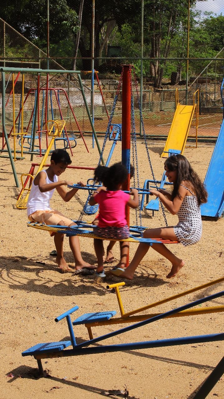Três crianças brincam em um carrossel em um playground de areia. As crianças puxam a roda e riem.