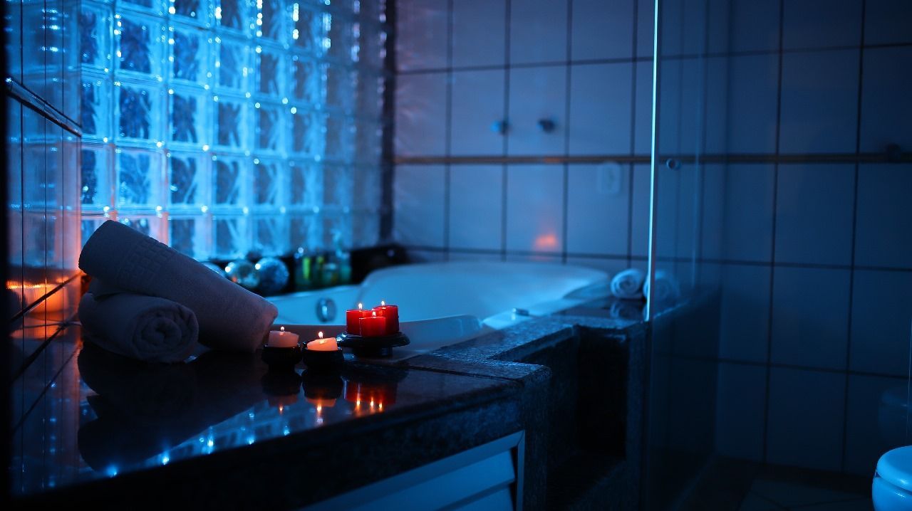 Um banheiro de spa com iluminação suave, jacuzzi aceso, velas e toalhas. O ambiente tem um tom azul.