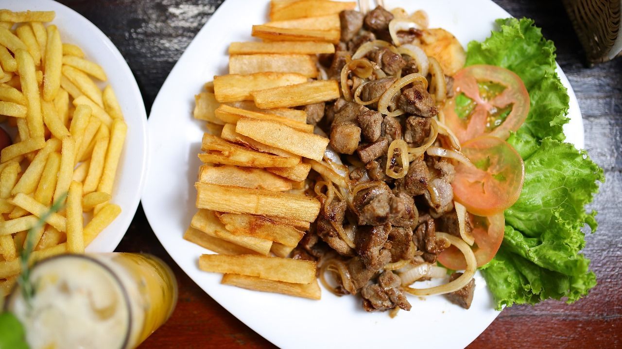 Prato de carne temperada com vegetais fritos, cebolas fatiadas, tomates e alface. Ao lado, um prato de batatas fritas.