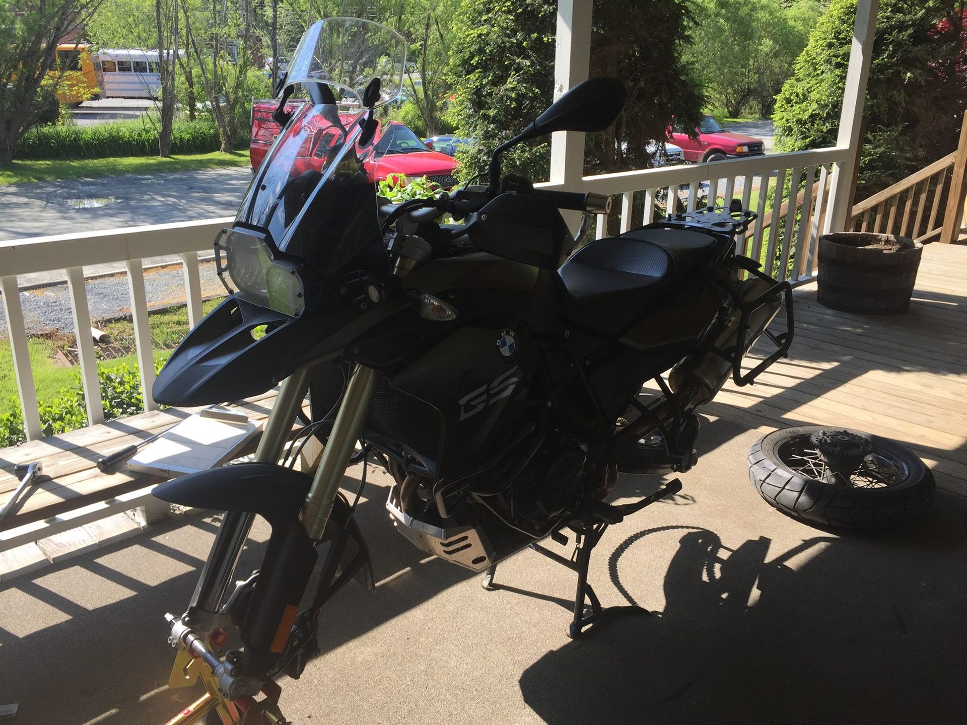 A black motorcycle is parked on a porch next to a tire.