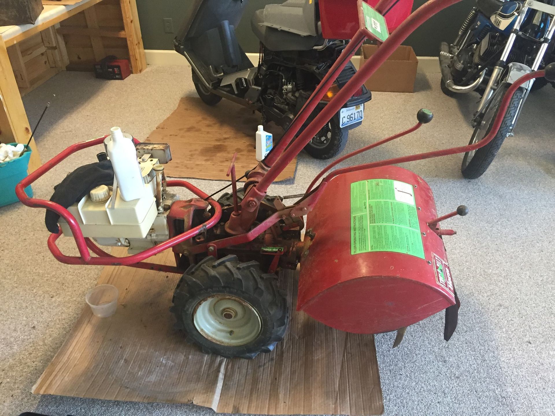 A small red tractor is sitting on a cardboard box in a garage.