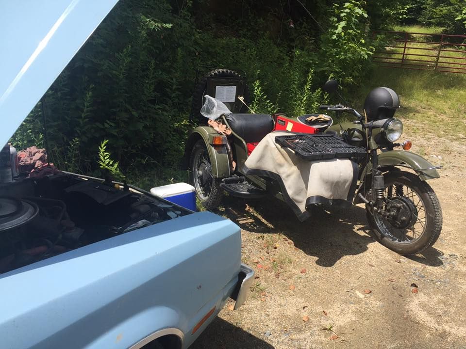 A motorcycle with a sidecar is parked next to a car with the hood open
