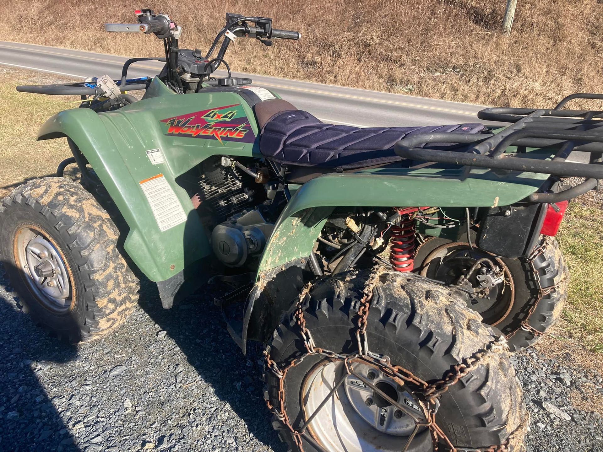 A green atv with chains on the tires is parked on the side of the road.