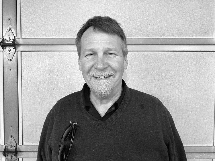 A man with a beard is smiling in front of a garage door.