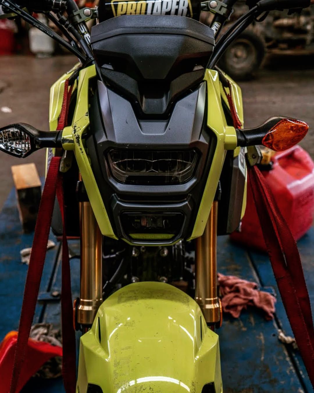 A yellow motorcycle is sitting on a table in a garage.