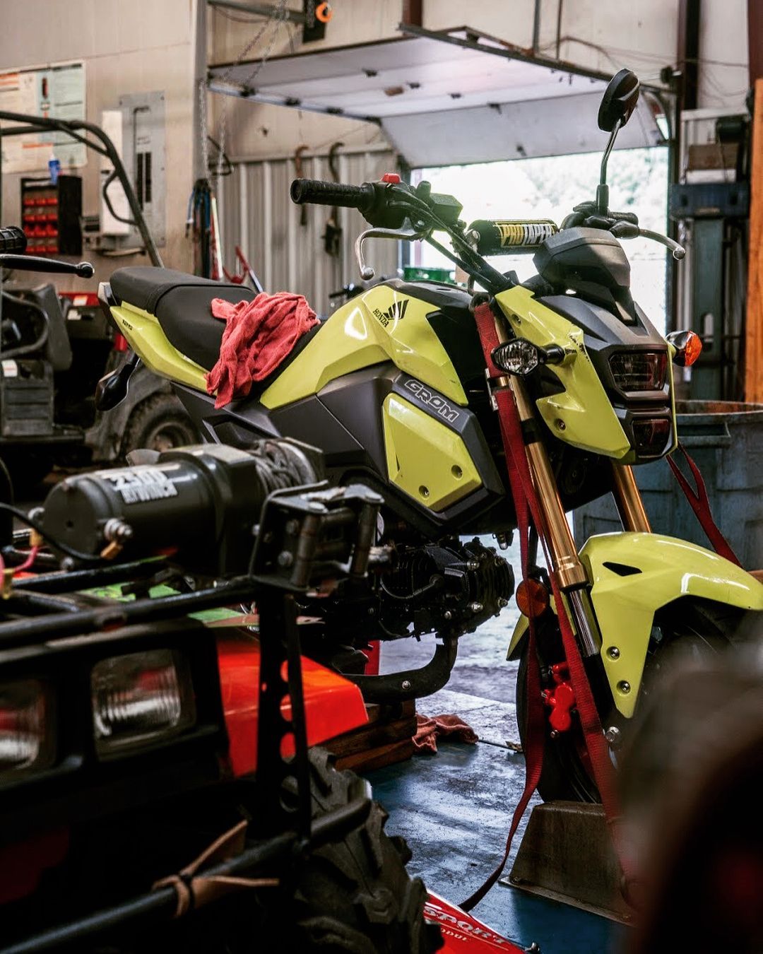 A yellow motorcycle is parked in a garage next to an atv