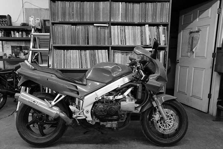 A black and white photo of a motorcycle parked in front of a bookshelf