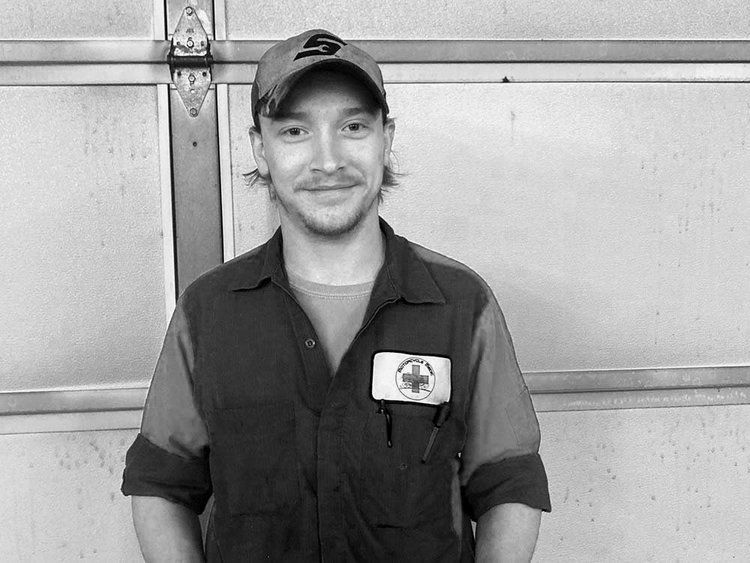 A man in a hat is standing in front of a garage door in a black and white photo.