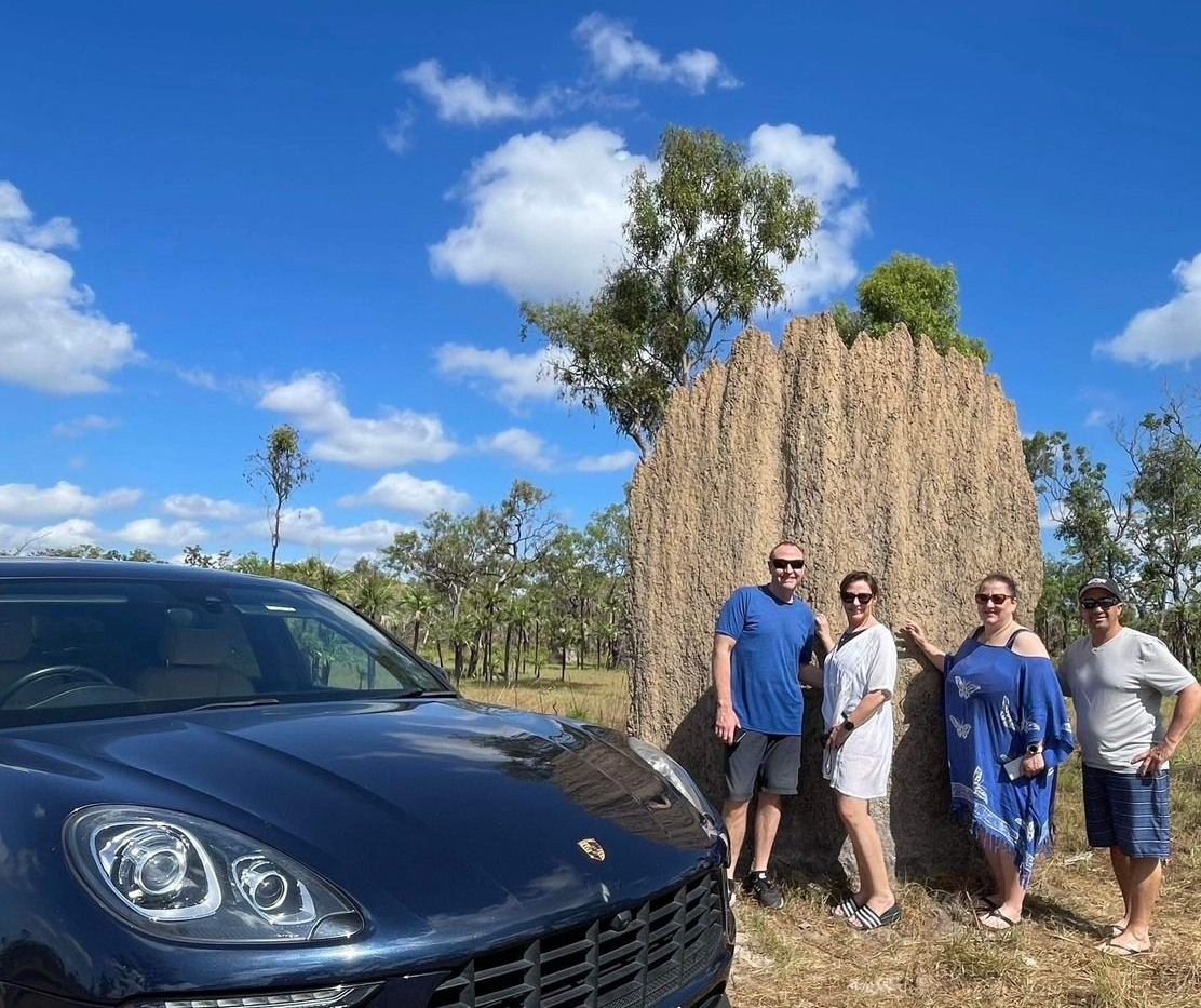 People pose next to a termite mound with a blue car, under a blue sky with clouds — Litchfield VIP Tours In Darwin City, NT