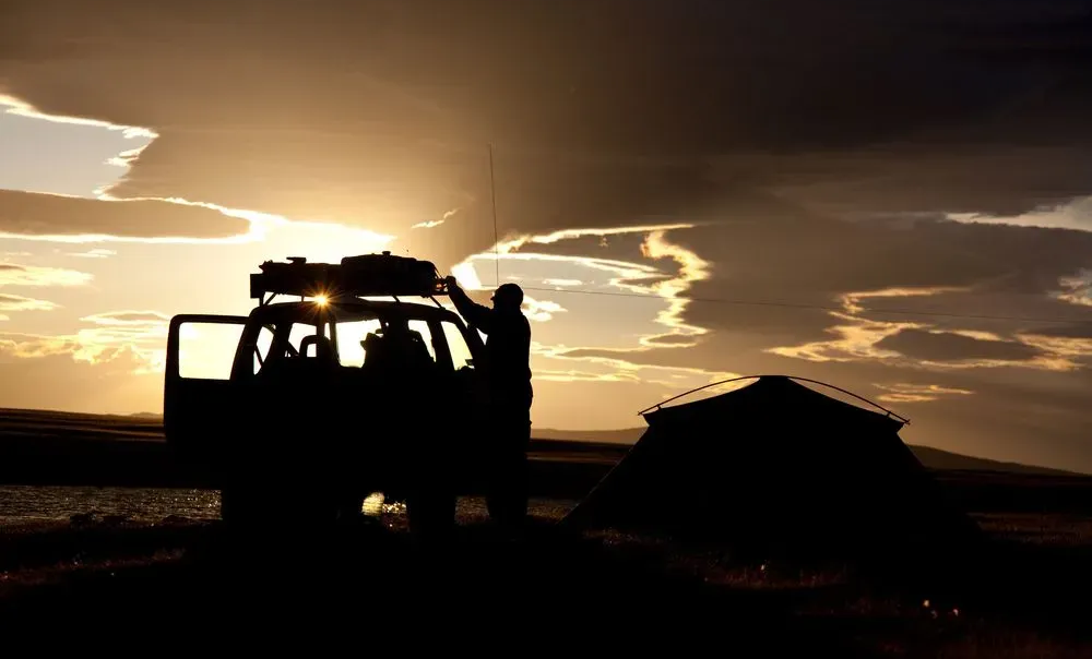 Silhouette of a Vehicle and Tent at Sunset With Person Adjusting Gear — Litchfield VIP Tours In Darwin City, NT