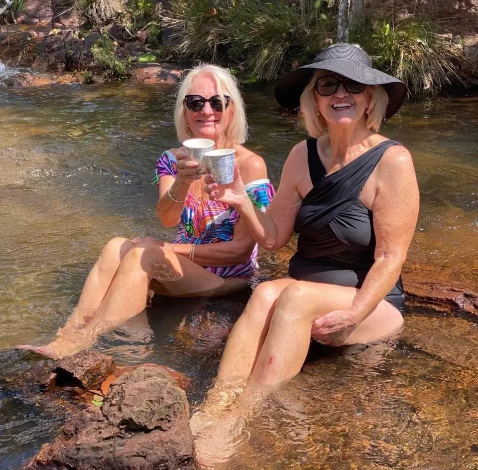 Two Women in Swimsuits Sitting in Water, Toasting With Cups, Smiling. Outdoors — Litchfield VIP Tours In Darwin City, NT