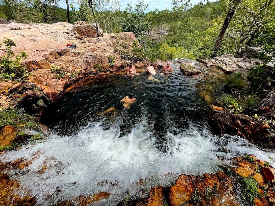 People Relaxing in a Natural Pool With Water Cascading Over Rocks — Litchfield VIP Tours In Darwin City, NT