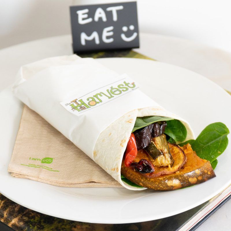 A Harvest vegetable wrap on a white plate with a napkin and a small sign reading