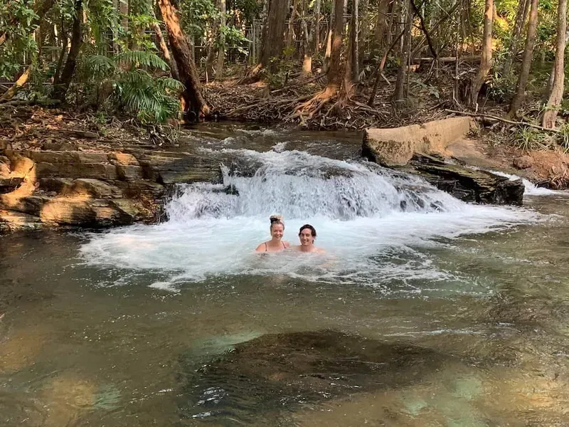 Two People Swim in a Clear Creek Near a Small Waterfall, Surrounded by Trees — Litchfield VIP Tours In Darwin City, NT