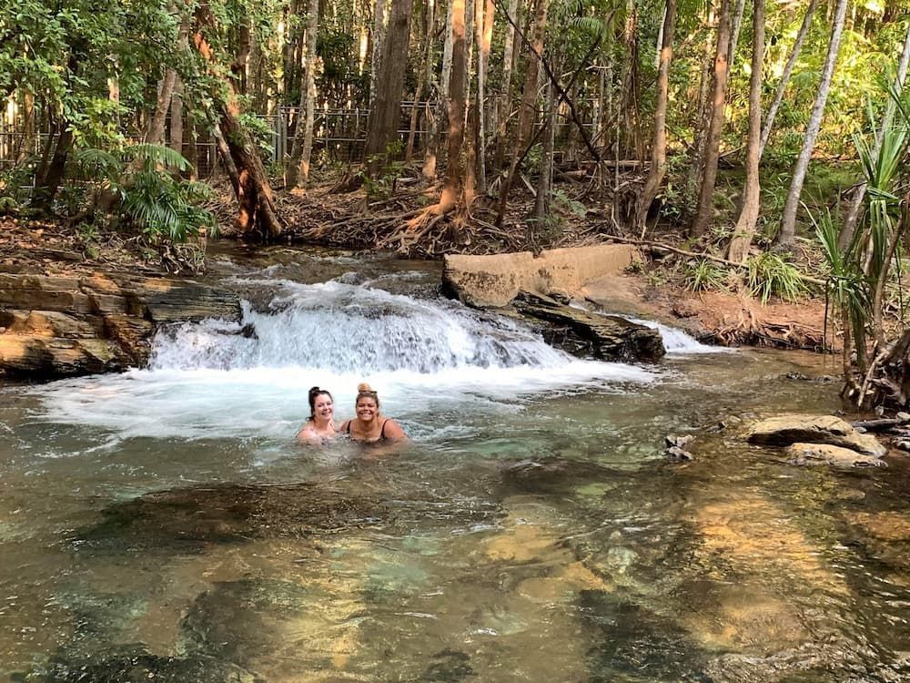 Two People Swim in a Clear Creek With a Small Waterfall, Surrounded by Trees — Litchfield VIP Tours In Darwin City, NT