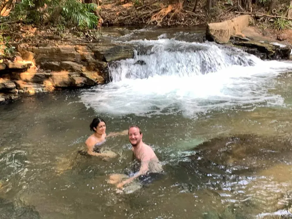 Couple Swimming in a Clear River With Small Waterfall, Smiling — Litchfield VIP Tours In Darwin City, NT