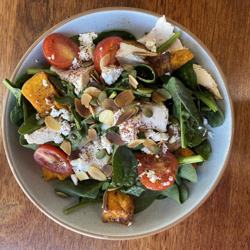 A bowl of salad featuring spinach, roasted pumpkin cubes, cherry tomatoes, white cheese, and nuts on a wooden table. — Litchfield VIP Tours In Darwin City, NT