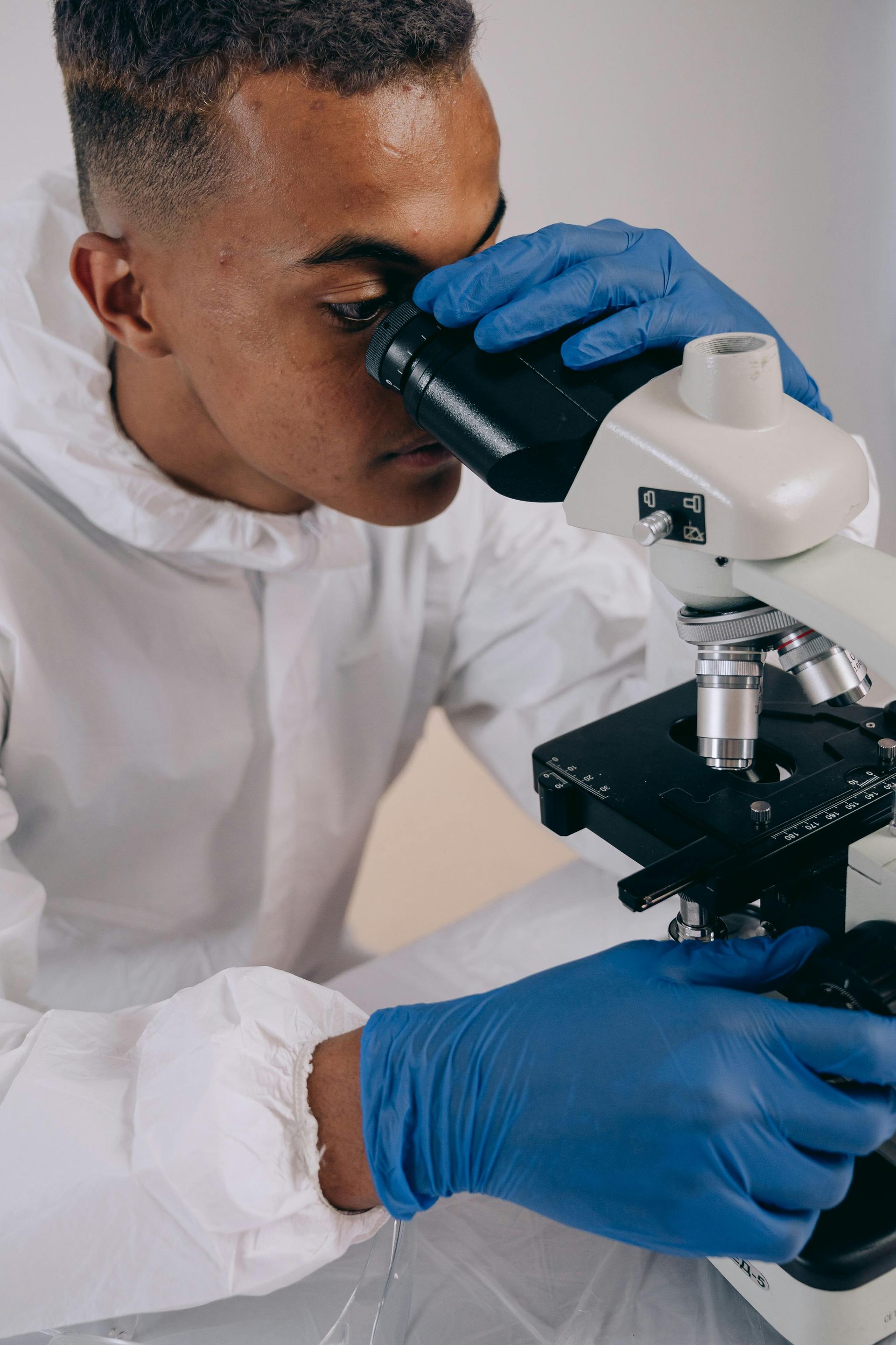 A Man Wearing Blue Gloves Is Looking Through A Microscope — Australian Asbestos Management Pty Ltd In Kunda Park, QLD