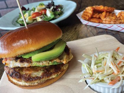 A sandwich with avocado and coleslaw is on a wooden cutting board.