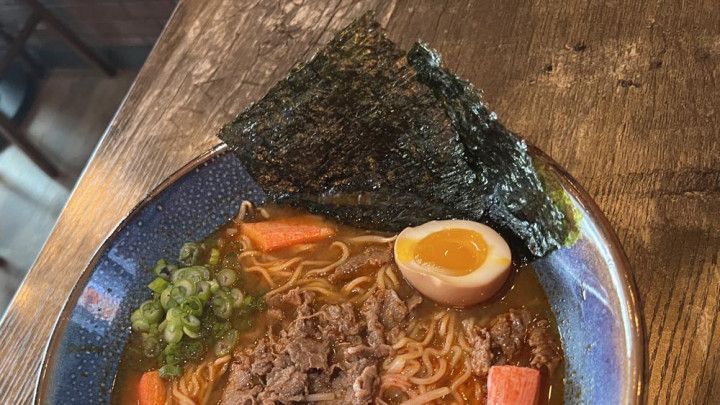 A bowl of ramen with beef , carrots , seaweed and an egg on a wooden table.