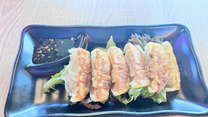 A black plate topped with fried dumplings and lettuce on a table.