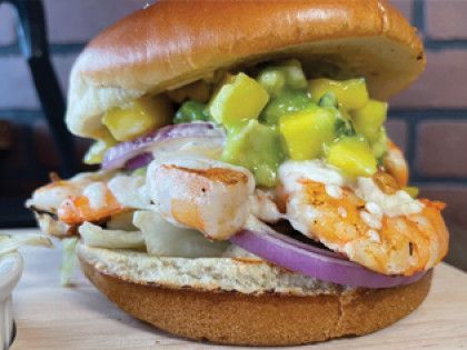 A close up of a shrimp sandwich on a bun on a wooden table.