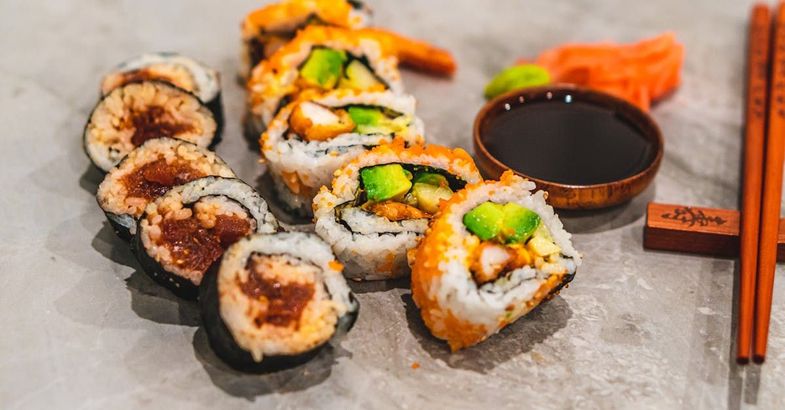 A plate of sushi with chopsticks and a bowl of soy sauce.