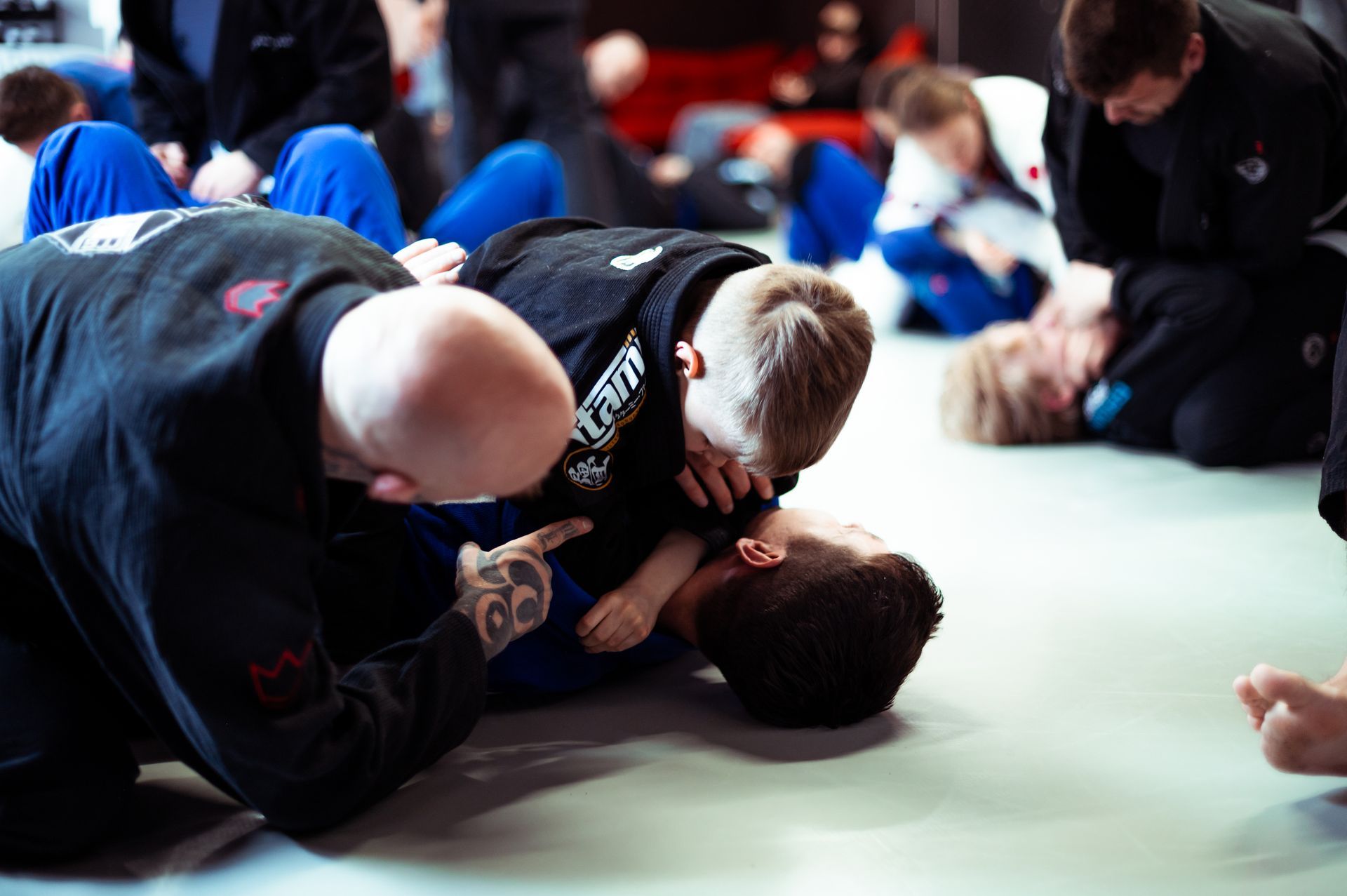 Zwei Kinder in Kampfsportanzügen stehen sich auf einer Matte gegenüber, andere Kinder schauen im Hintergrund zu.