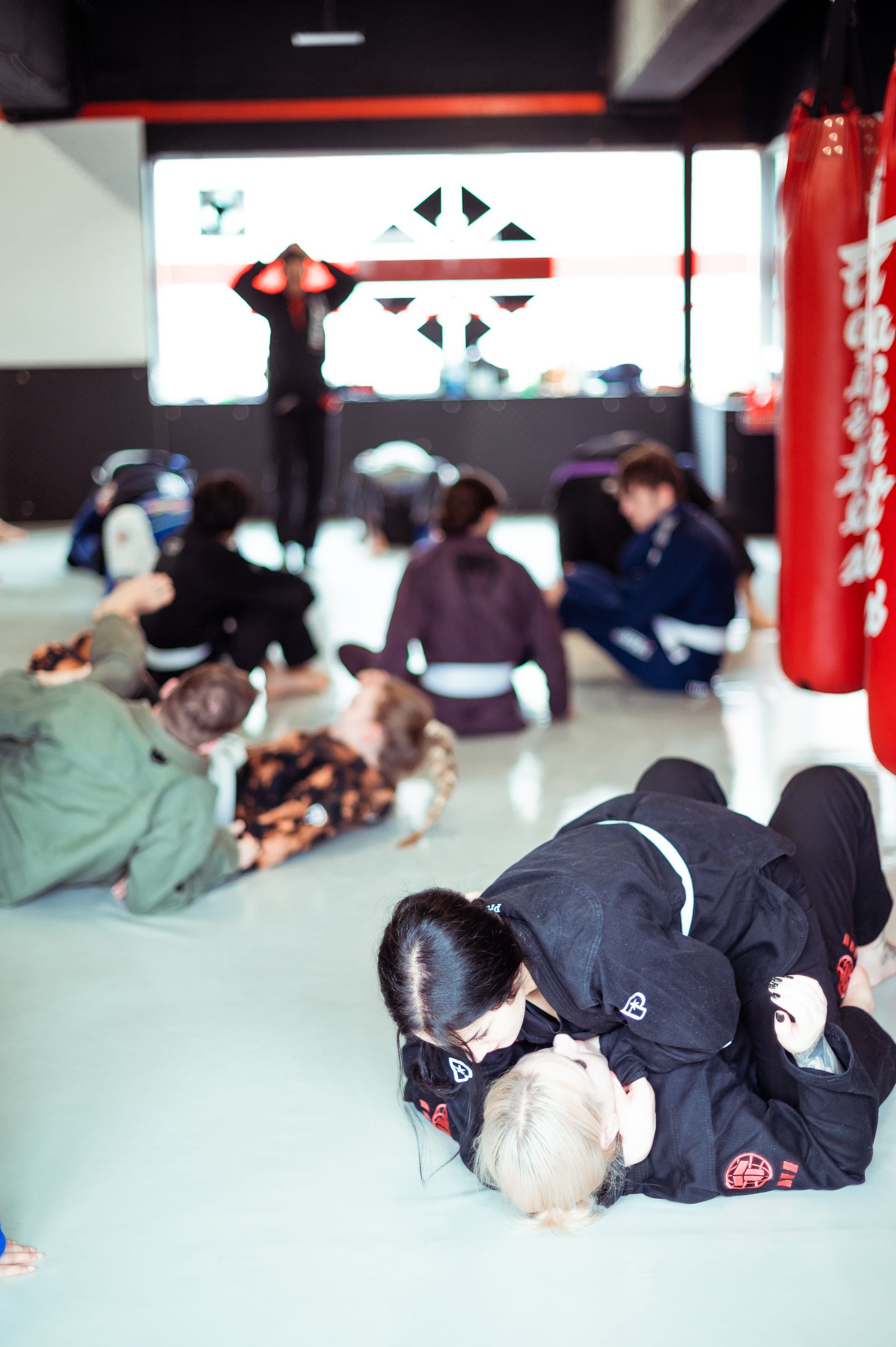 Zwei Personen üben Kampfsport: Eine Person hebt die andere, die sich vornübergebeugt hat, in einem Studio hoch.
