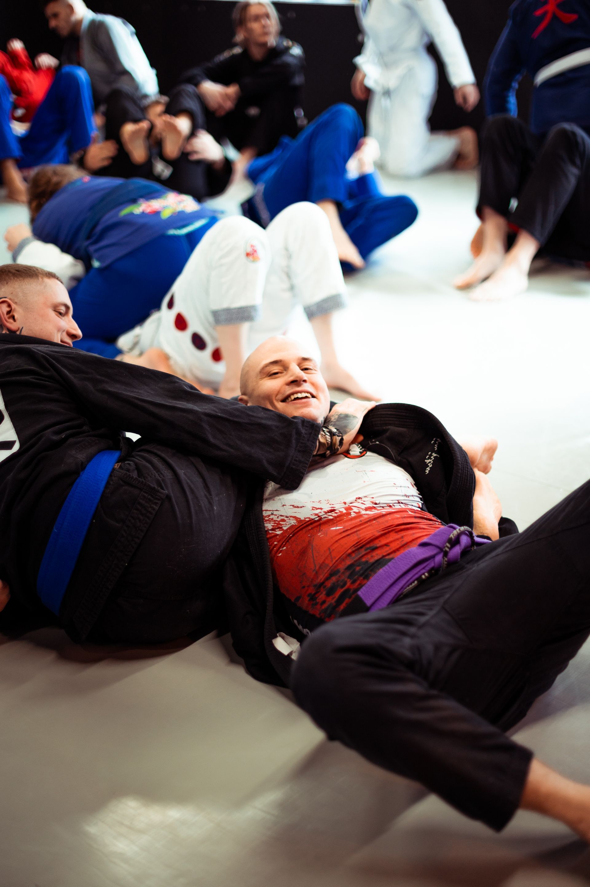 Ein Mann in blau-beigem Gi liegt auf einer Matte in einem Würgegriff. Sein Gesichtsausdruck verrät Anspannung.