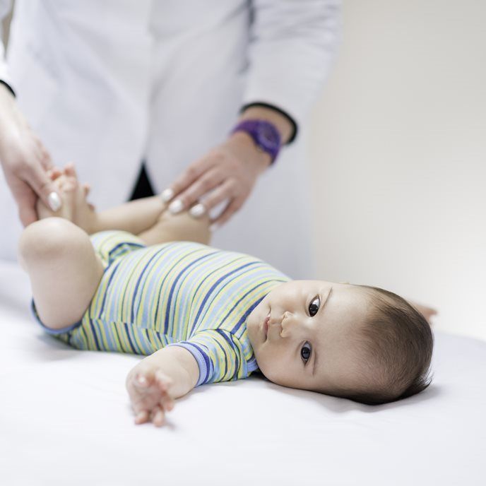 A healthcare professional in a white coat examines a baby lying on an exam table.
