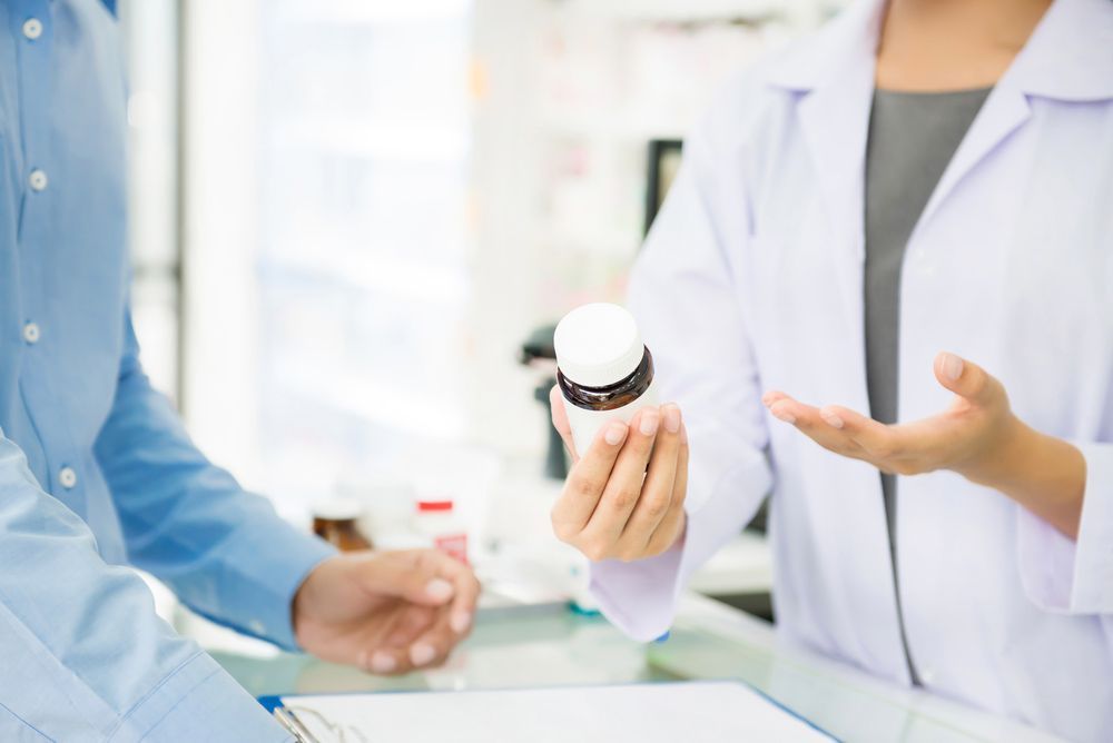Female Pharmacist Holding Medicine Bottle Giving Advice To Customer In Pharmacy — Return Unwanted Medicines in Wulguru, QLD