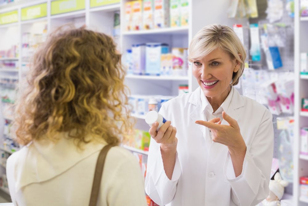 Pharmacist Holding A Bottle Of Drugs Talking To Customer In The Pharmacy — Scripts on File & E-Scripts in Wulguru, QLD