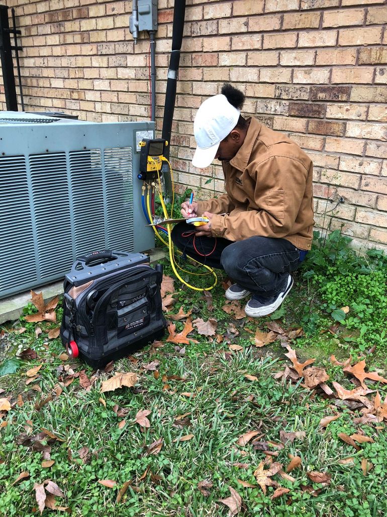 A man is working on an air conditioner outside of a brick building.