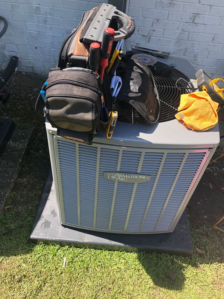 An air conditioner with a tool bag on top of it.