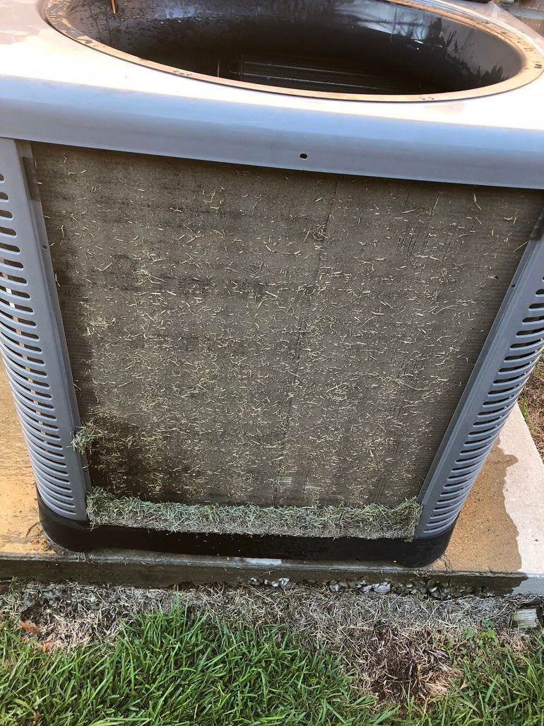 A dirty air conditioner is sitting on a sidewalk next to a grassy area.