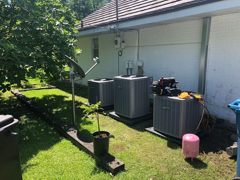 A row of air conditioners are sitting on the grass in front of a house.