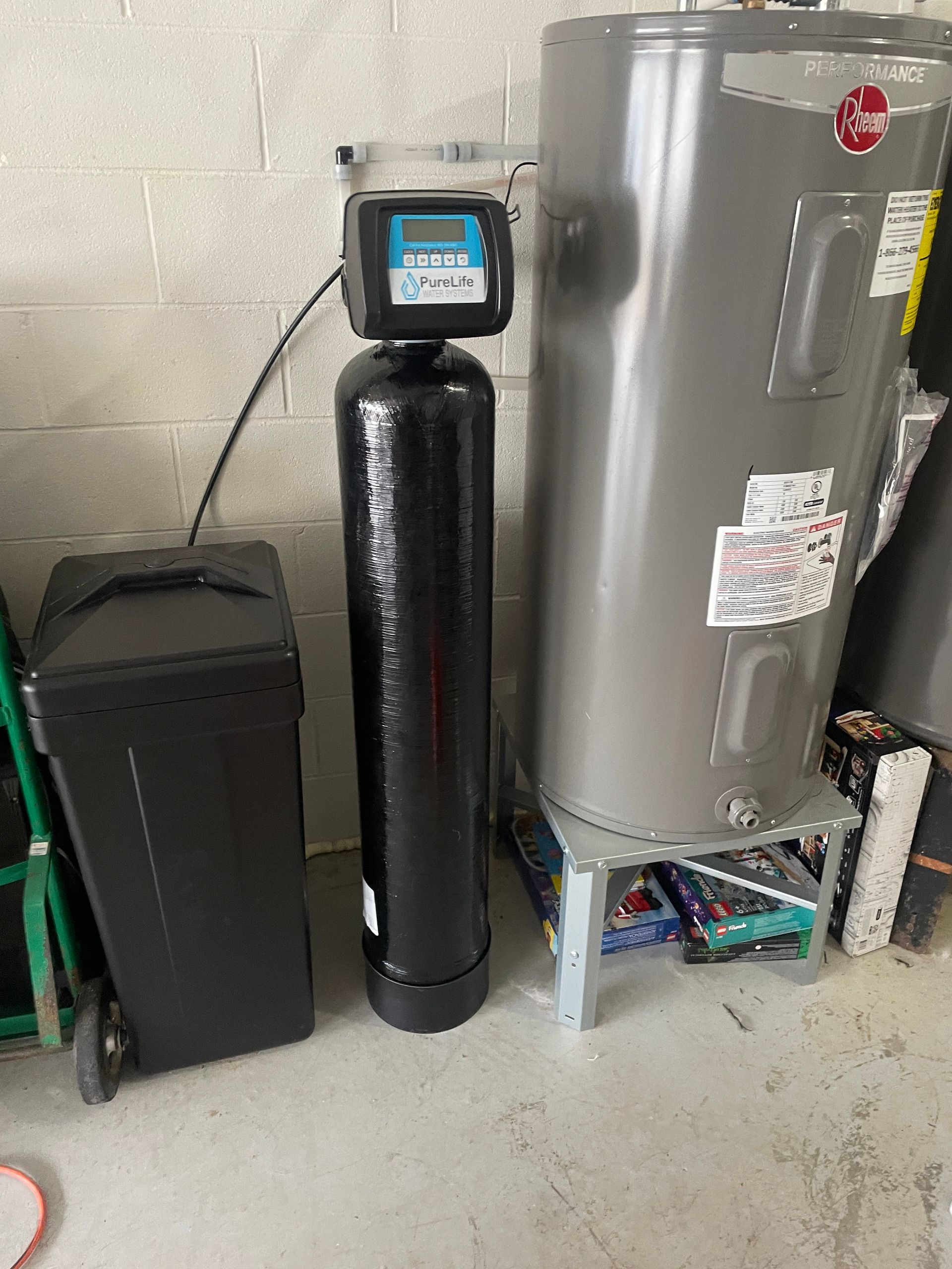 A water softener is sitting next to a water heater in a garage.