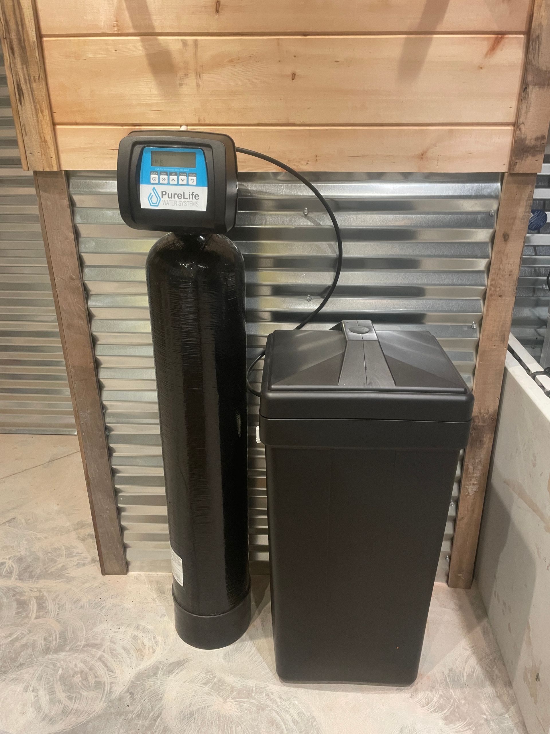 A water softener is sitting next to a trash can in a room.