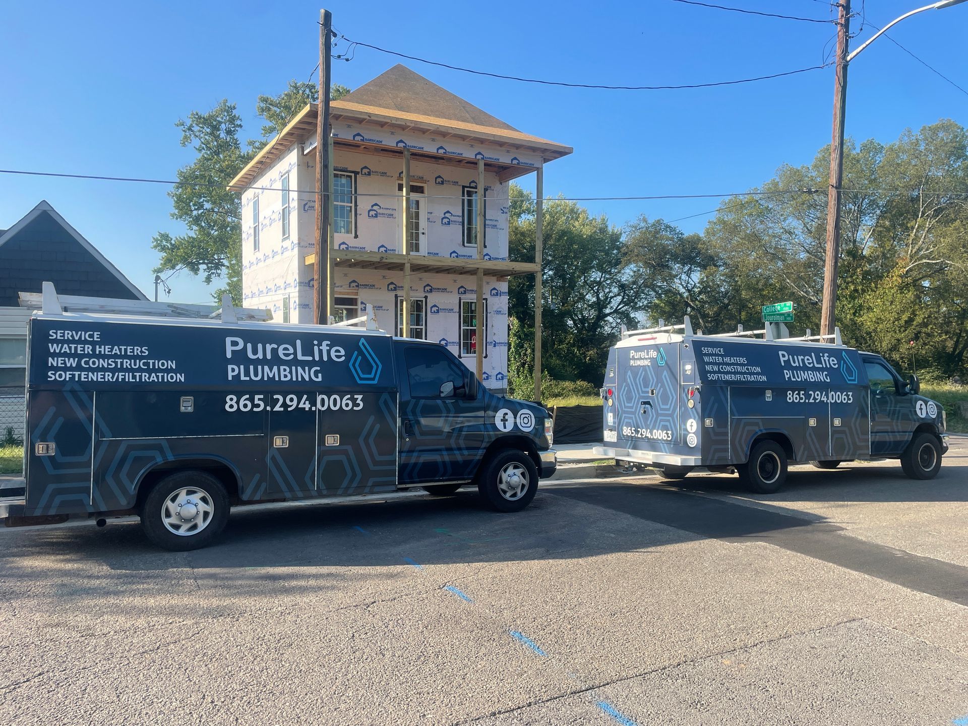 Two plumbing vans are parked in front of a house under construction.