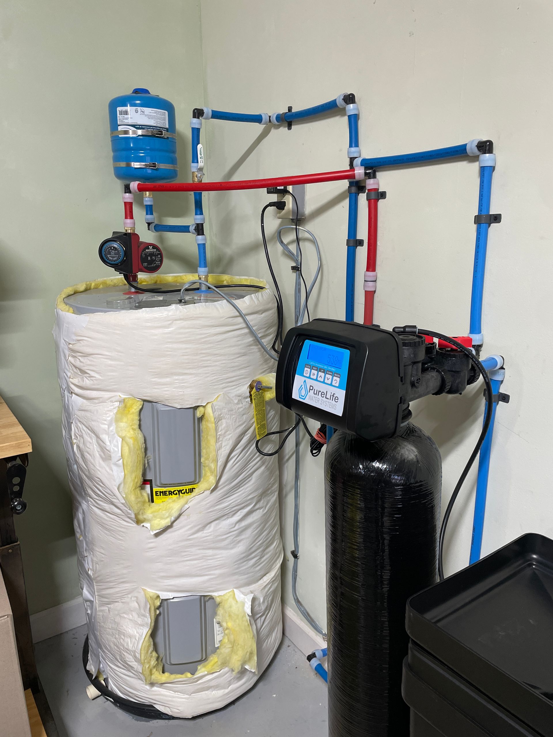 A water heater is sitting in a room next to a water softener.