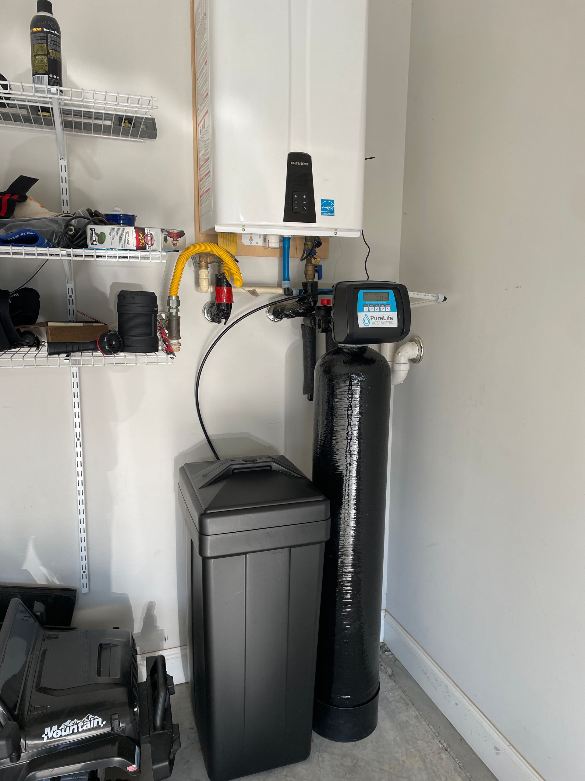 A water softener is sitting next to a boiler in a garage.