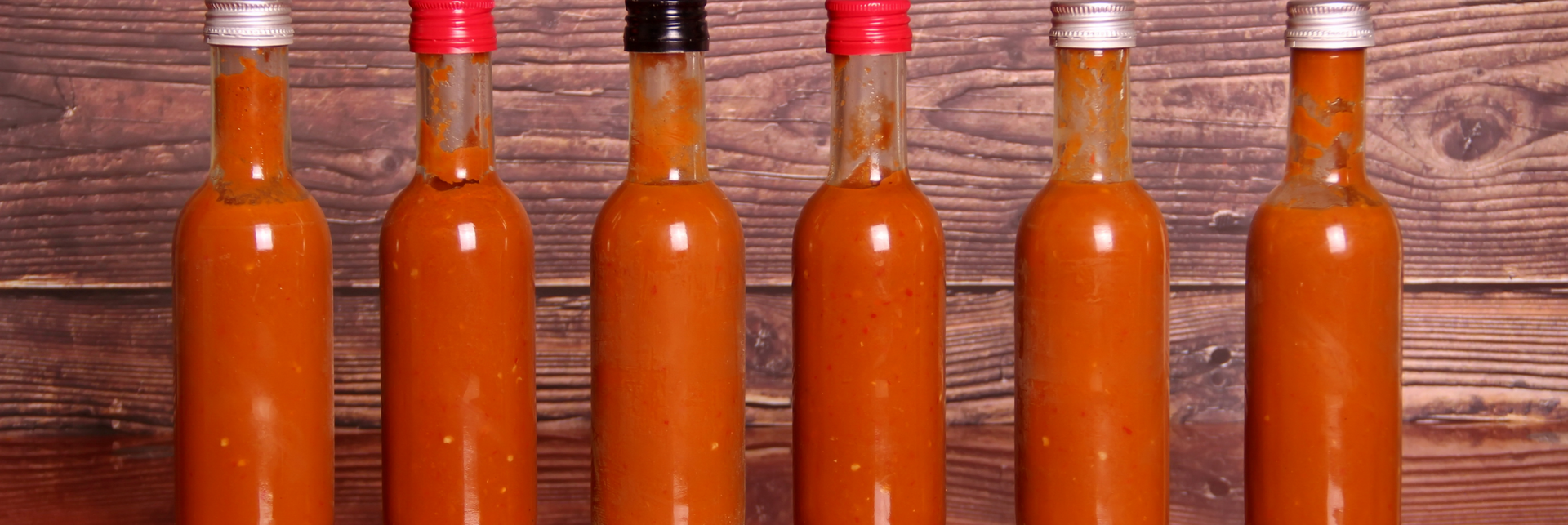 Five bottles of hot sauce are lined up on a wooden table.